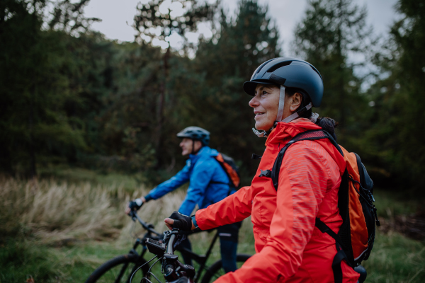 A senior couple bikers with e-bikes admiring nature outdoors in forest in autumn day.