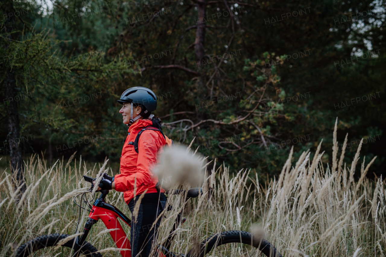 A senior woman biker walking with bike outdoors in nature in autumn day.