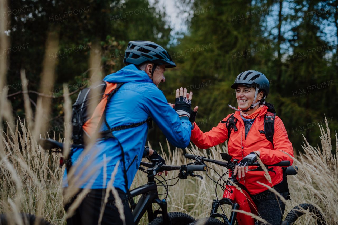 A senior couple bikers high fiving outdoors in forest in autumn day.