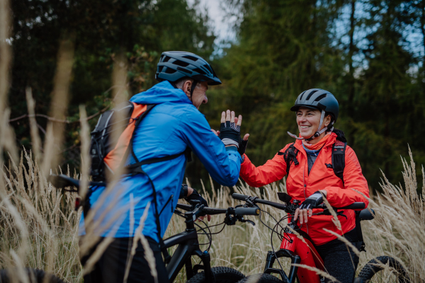 A senior couple bikers high fiving outdoors in forest in autumn day.