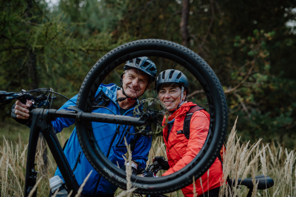 An active senior couple mending bicycle outdoors in forest in autumn day.