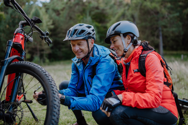 An active senior couple mending bicycle outdoors in forest in autumn day.