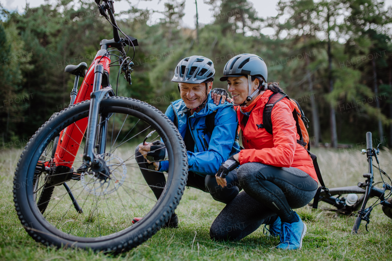 An active senior couple mending bicycle outdoors in forest in autumn day.