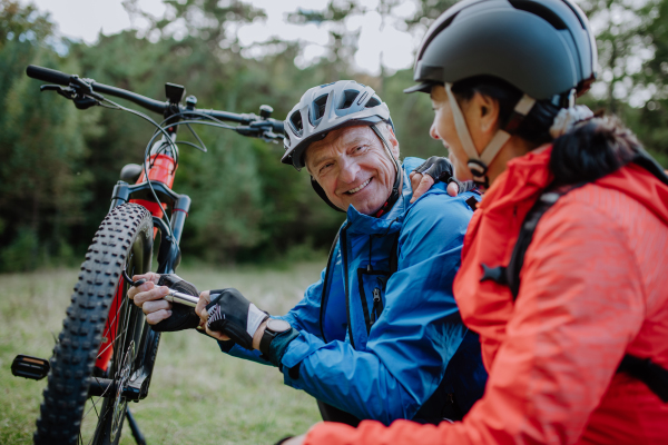 An active senior couple mending bicycle outdoors in forest in autumn day.