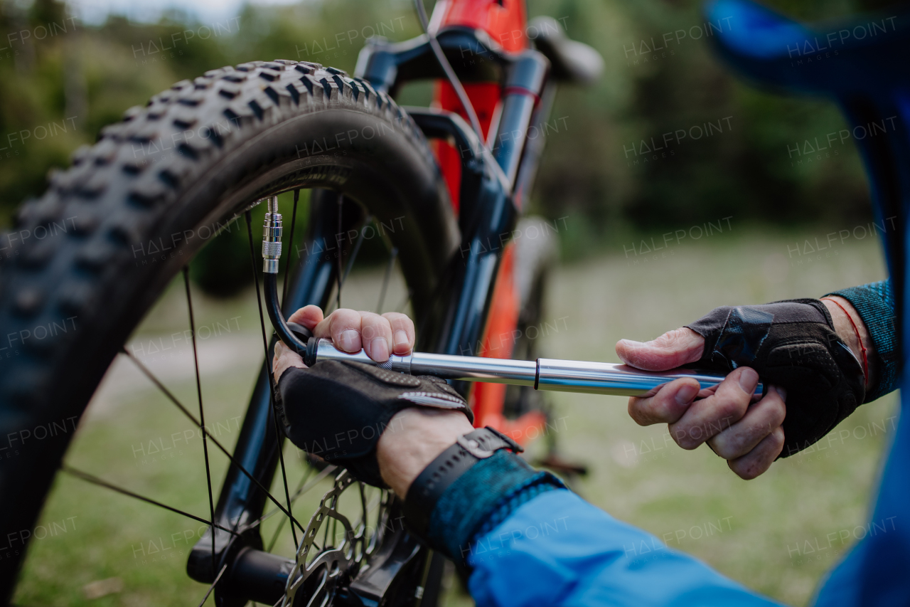 A close-up of a man pumping bicycle wheel in nature.