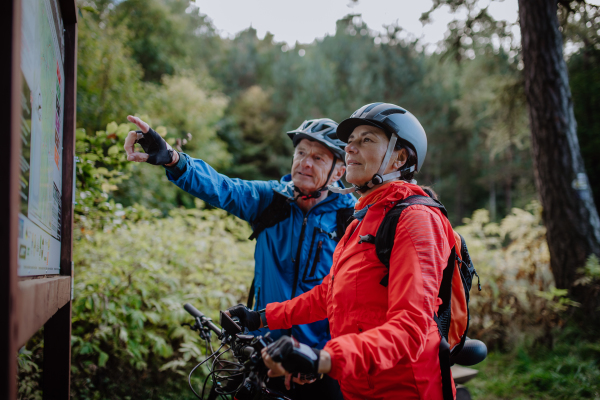 A happy senior couple bikers looking at map outdoors in nature in autumn day.