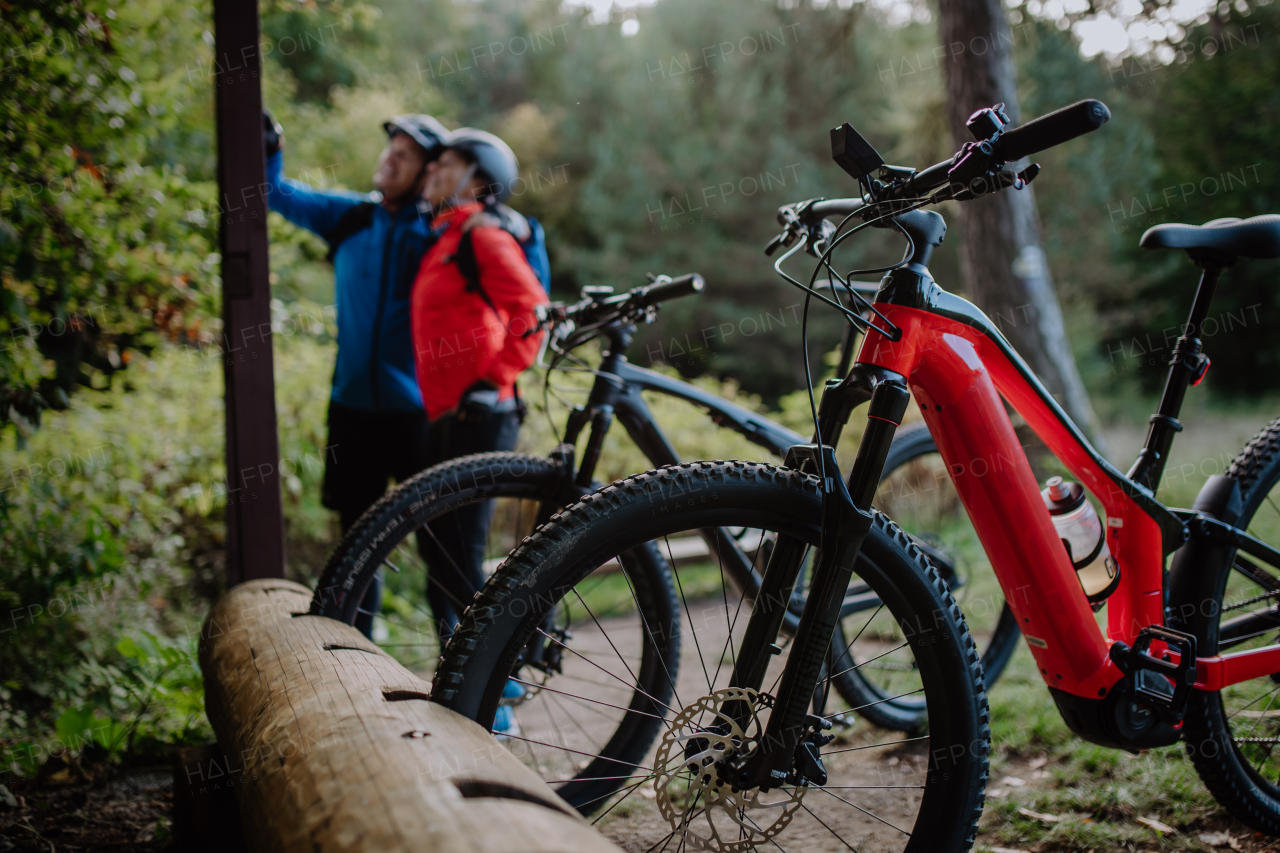 A happy senior couple bikers resting outdoors in nature in autumn day, detail on bikes.