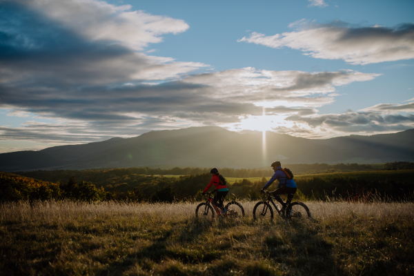 An active senior couple riding bikes outdoors in autumn nature at dusk.