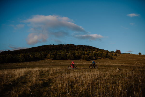 A side view of active senior couple riding bikes outdoors in forest in autumn day.