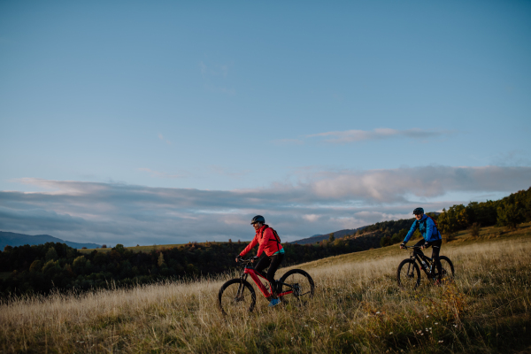 A side view of active senior couple riding bikes outdoors in countryside in autumn day.