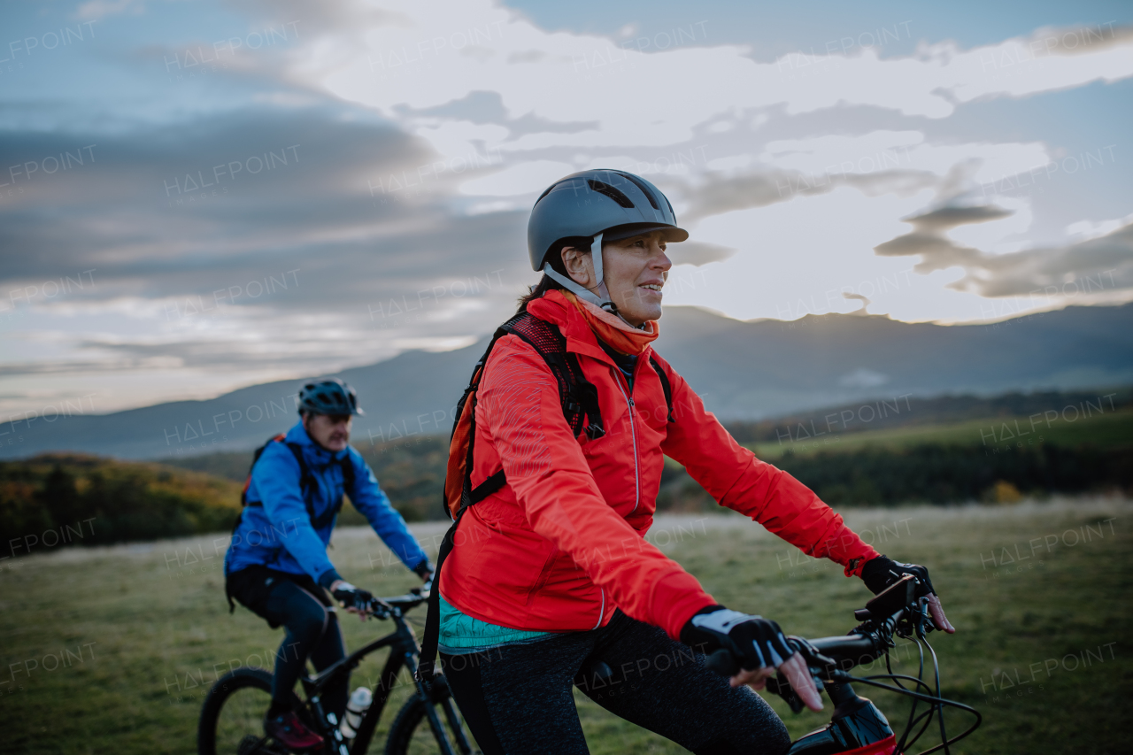 An active senior couple riding bikes outdoors in forest in autumn day.