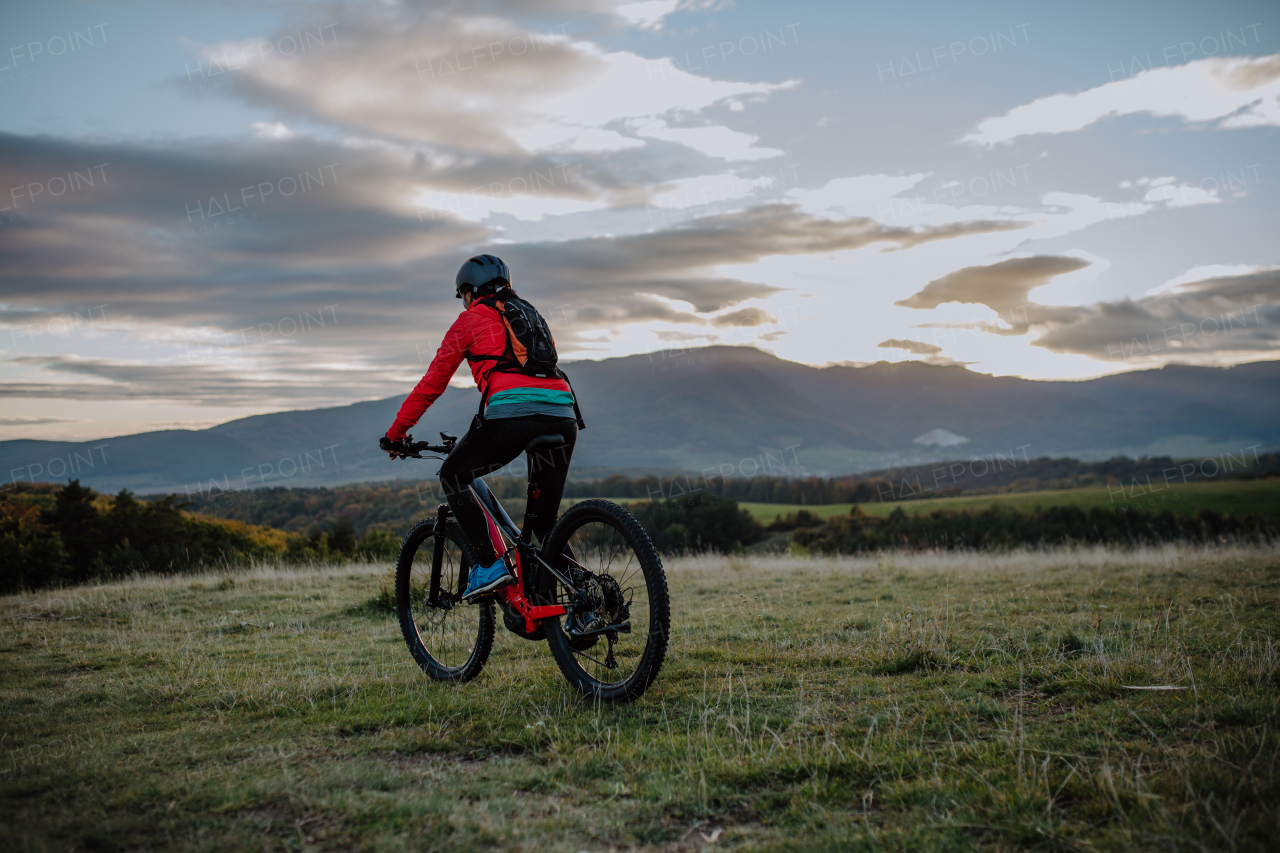 A rear view of active senior woman biker riding bike in nature on autumn day.