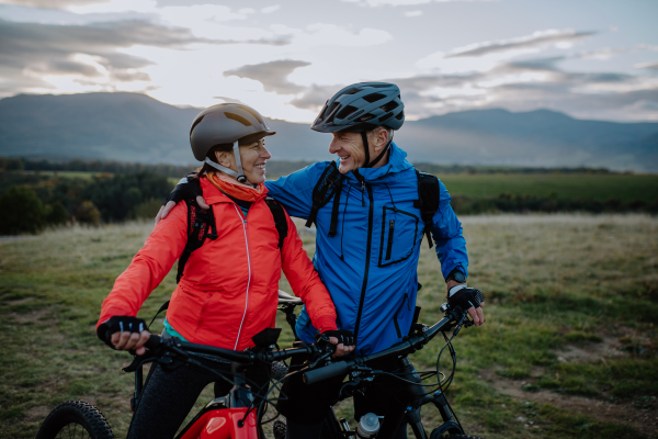 A happy senior couple bikers wmbracing outdoors in nature in autumn day.