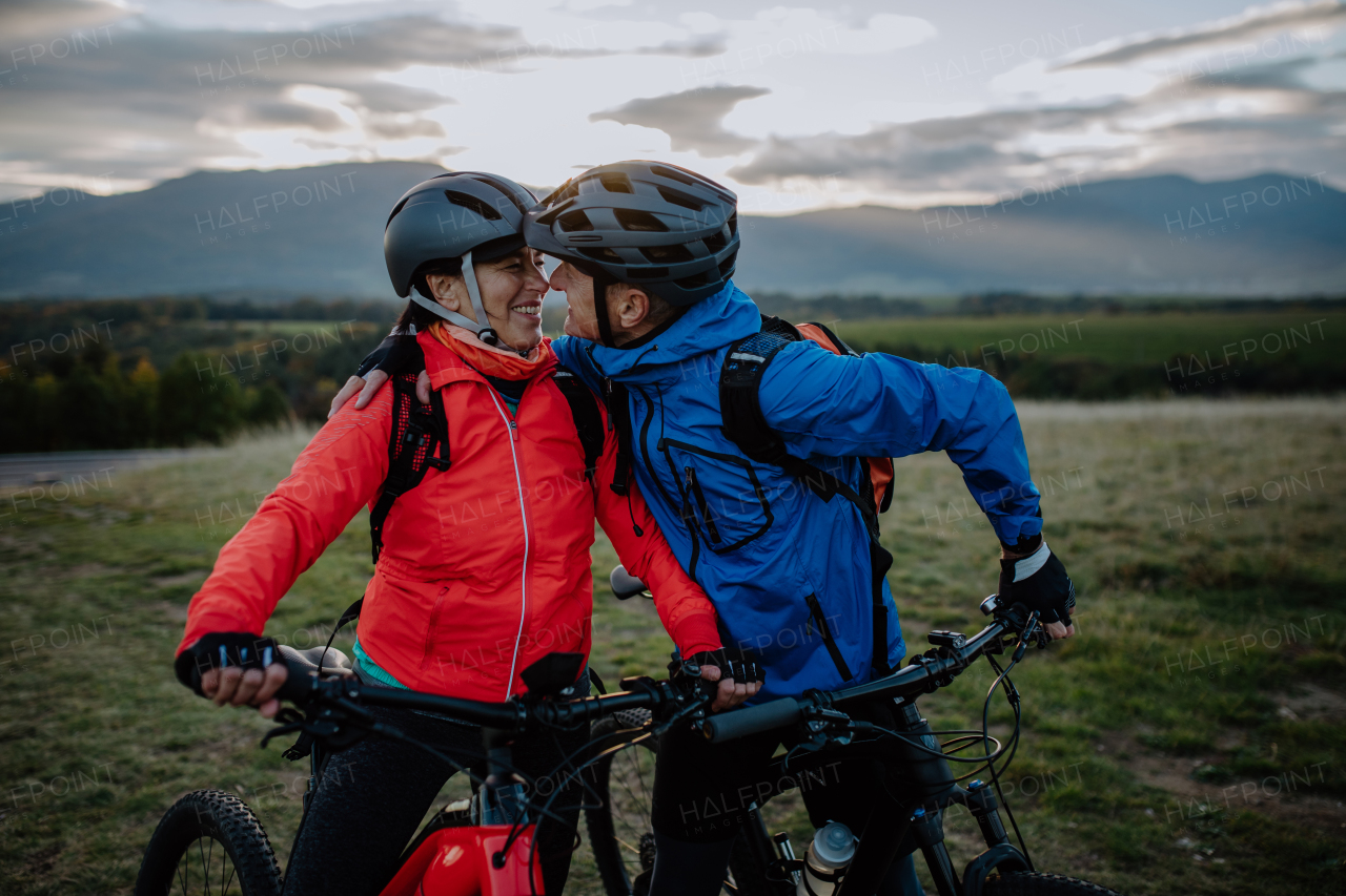 A happy senior couple bikers embracing and looking at each other outdoors in nature in autumn day.