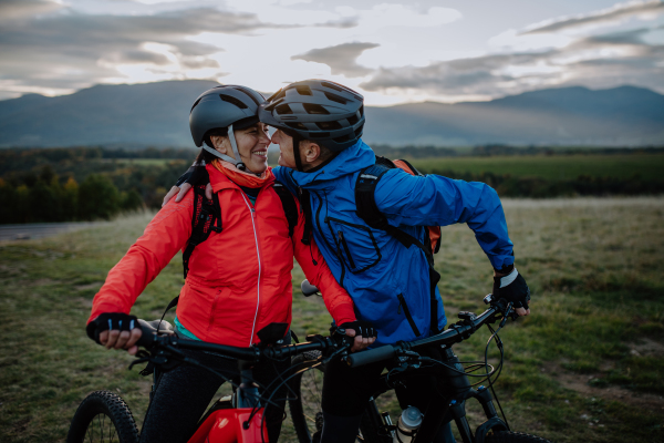 A happy senior couple bikers embracing and looking at each other outdoors in nature in autumn day.