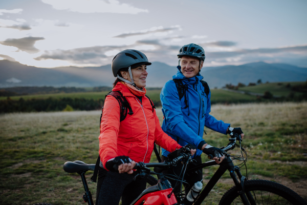 A senior couple bikers admiring nature outdoors in meadow in autumn day.