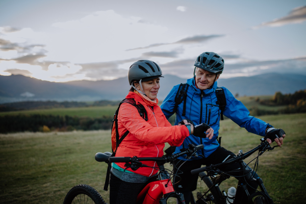 A senior couple bikers setting smartwatch outdoors in forest in autumn day.