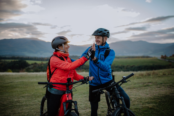 A senior couple bikers high fiving outdoors in forest in autumn day.