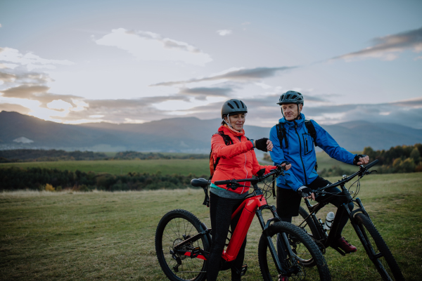 A senior couple bikers setting smartwatch outdoors in forest in autumn day.