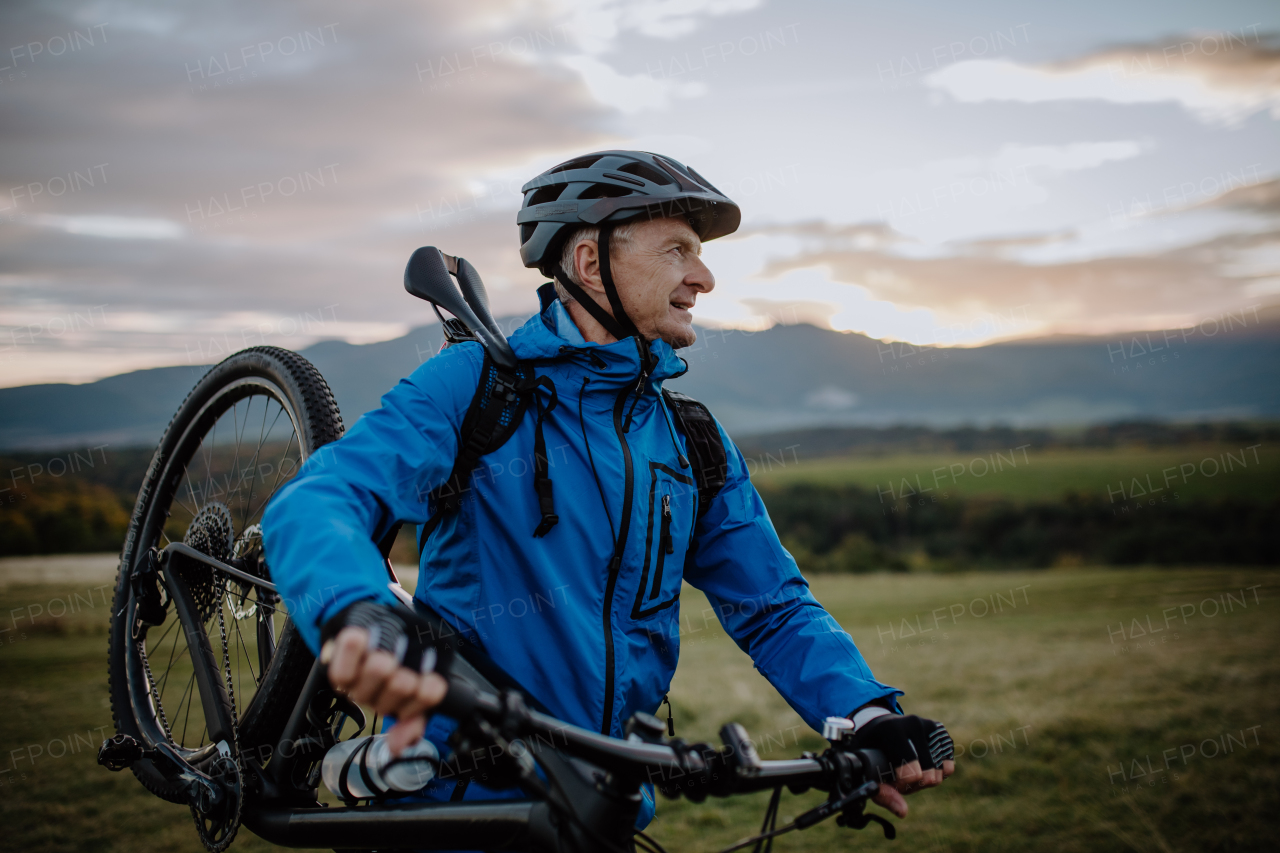 An active senior man biker carrying his bike outdoors in nature in autumn day.