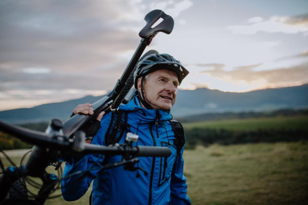 An active senior man biker carrying his bike outdoors in nature in autumn day.