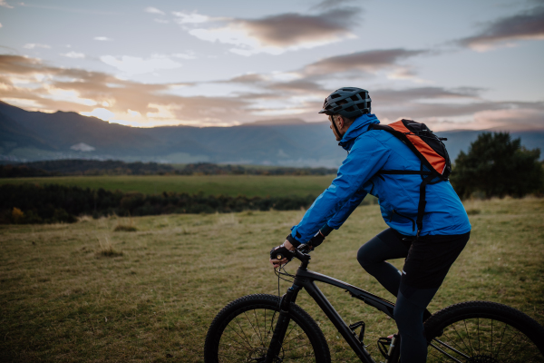 A side view of active senior man biker riding bike in nature on autumn day.