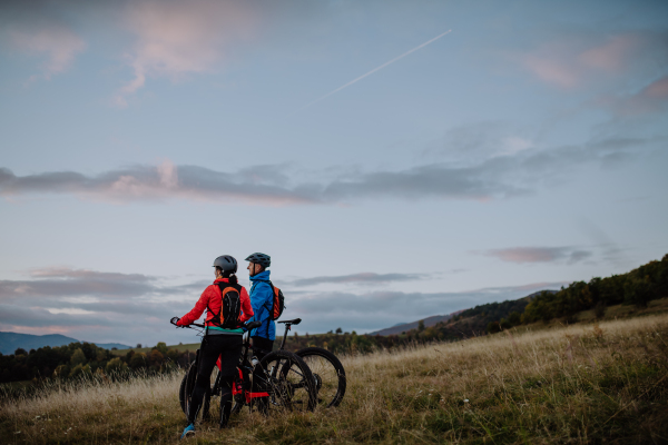 A senior couple bikers with e-bikes admiring nature outdoors in forest in autumn day.