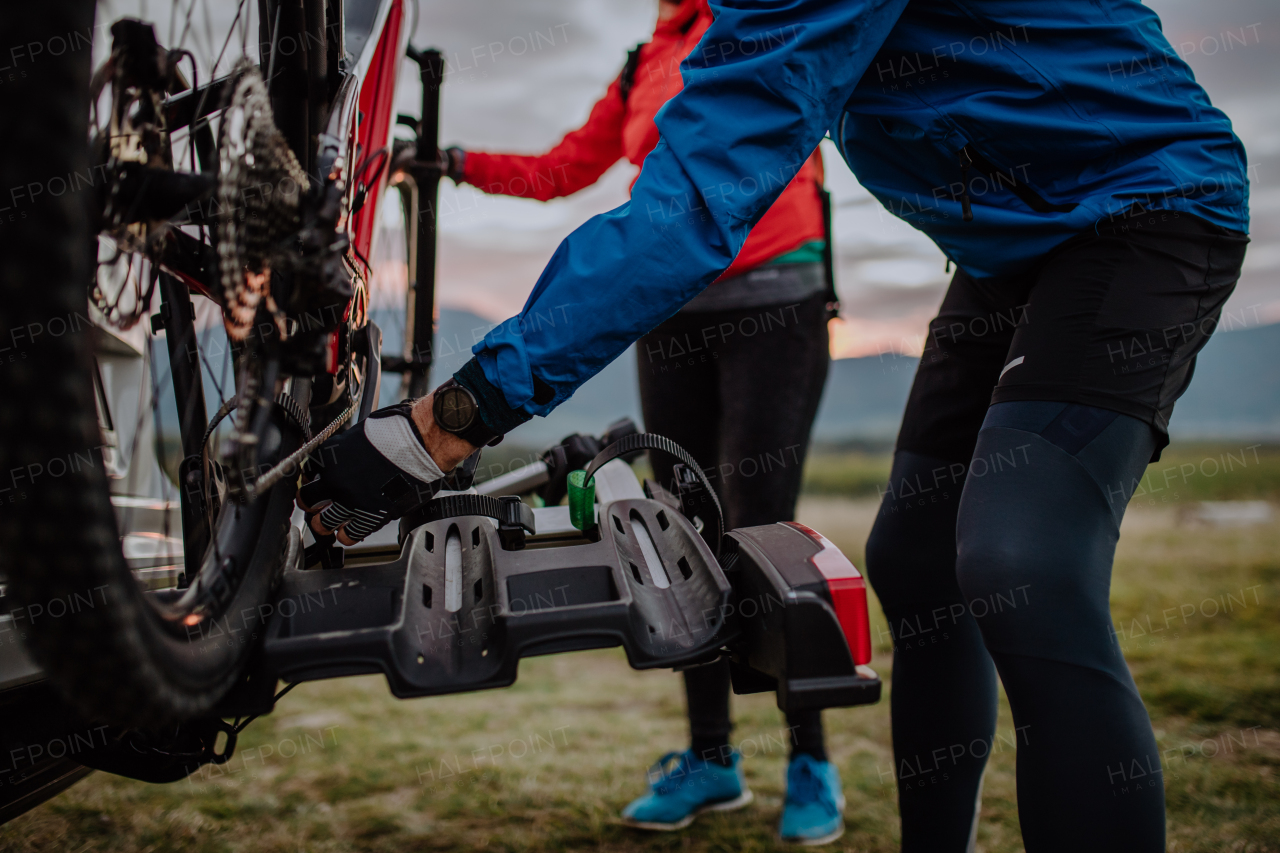 An active senior couple loading their bicycles on car carrier outdoors in nature in autumn day.