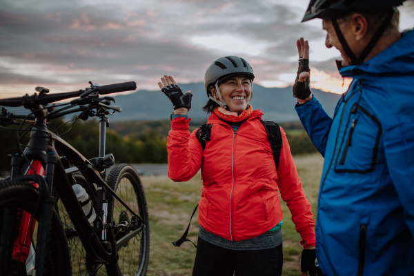 A senior couple bikers high fiving outdoors in forest in autumn day.