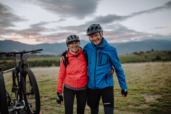 A senior couple bikers looking at camera outdoors in nature in autumn day.