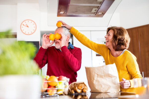 Senior couple unpacking food in the kitchen. An old man and woman inside the house, having fun.