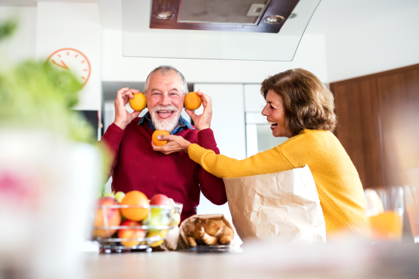 Senior couple unpacking food in the kitchen. An old man and woman inside the house, having fun.