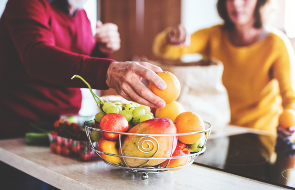 Unrecognizable senior couple unpacking fruit in the kitchen. An old man and woman inside the house.