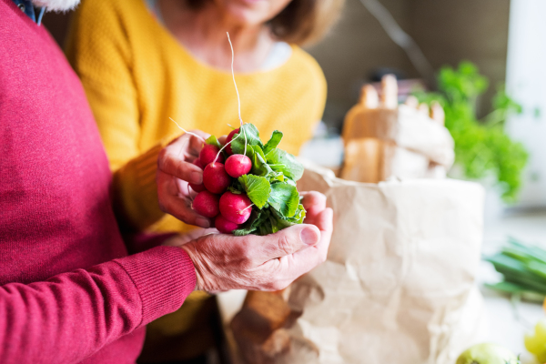 Unrecognizable senior couple unpacking food in the kitchen. An old man and woman inside the house.