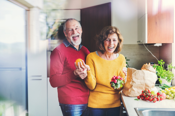 Senior couple unpacking food in the kitchen. An old man and woman inside the house. Shot through glass.