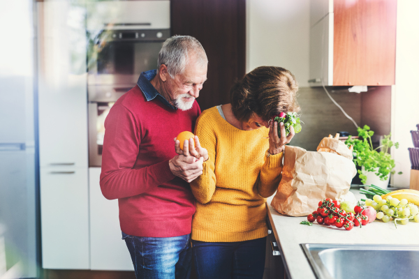 Senior couple unpacking food in the kitchen. An old man and woman inside the house. Shot through glass.