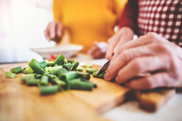 Unrecognizable senior man and woman preparing food in the kitchen. An old man chopping vegetables.