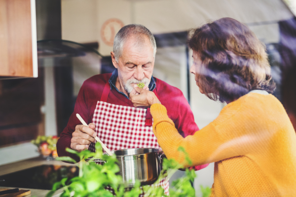 Senior couple preparing food in the kitchen. An old man and woman inside the house. Shot through glass.