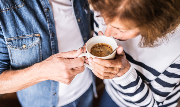 Senior couple talking in the kitchen. Unrecognizable old man and woman inside the house, holding a cup of coffee.