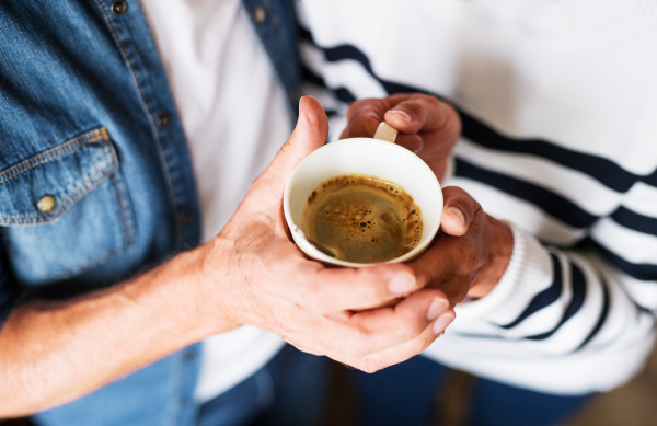 Unrecognizable senior couple at home. An old man and woman inside the house, holding a cup of coffee. Top view.