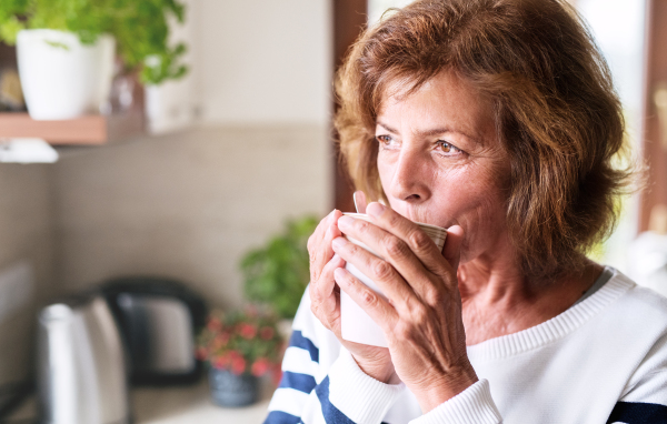 Senior woman in the kitchen. An old woman inside the house, holding and drinking a cup of coffee.