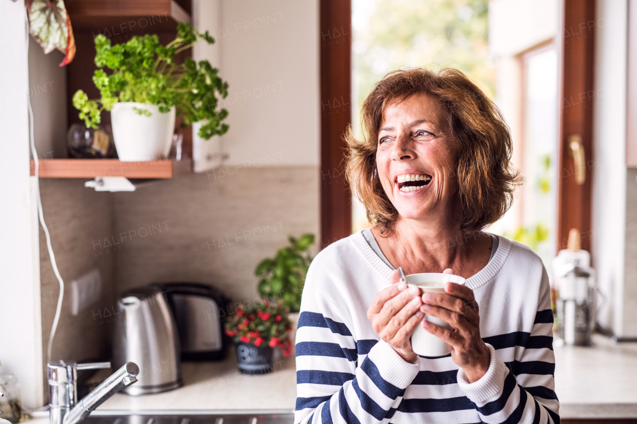 Senior woman in the kitchen. An old woman inside the house, holding a cup of coffee.