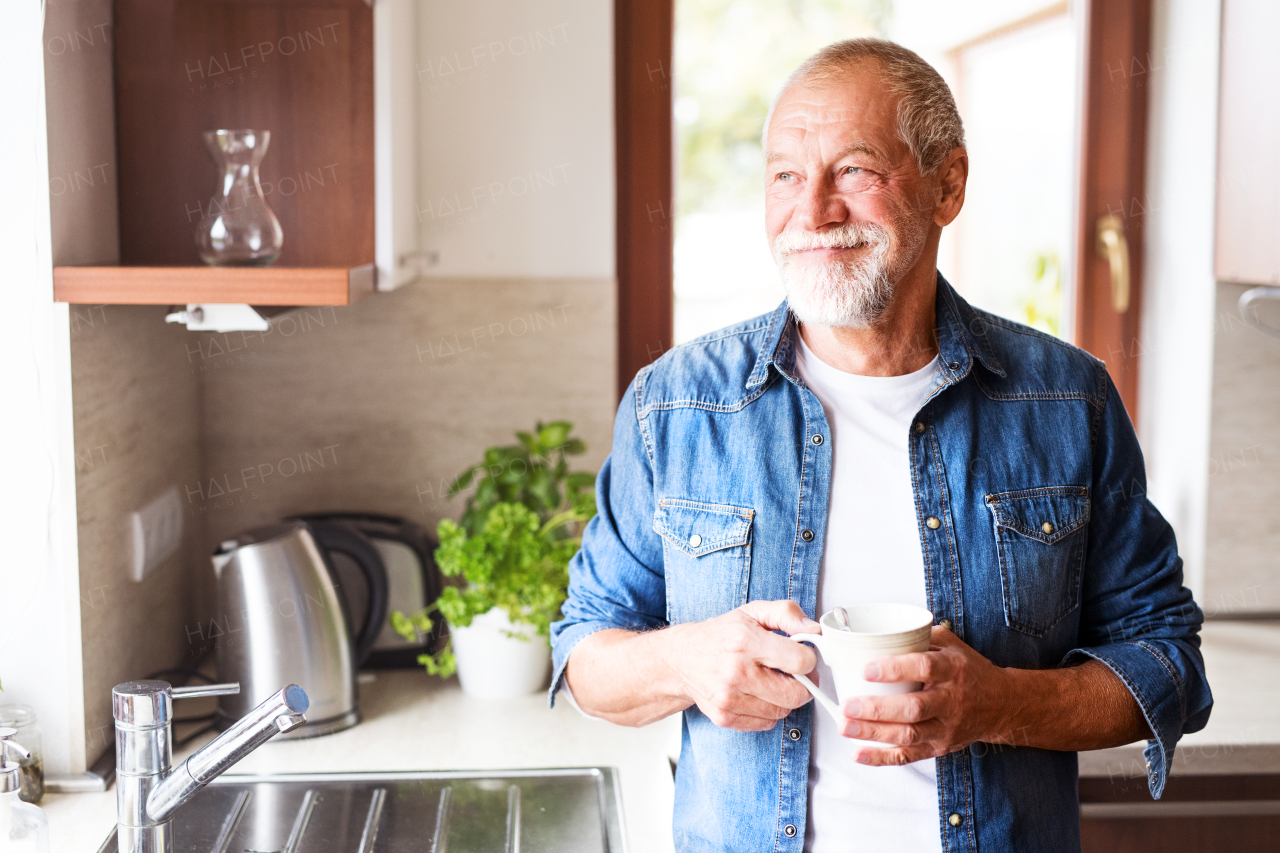 Happy senior man in the kitchen. An old man inside the house, holding a cup of coffee.