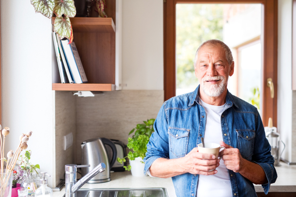 Senior man in the kitchen. An old man inside the house, holding a cup of coffee.