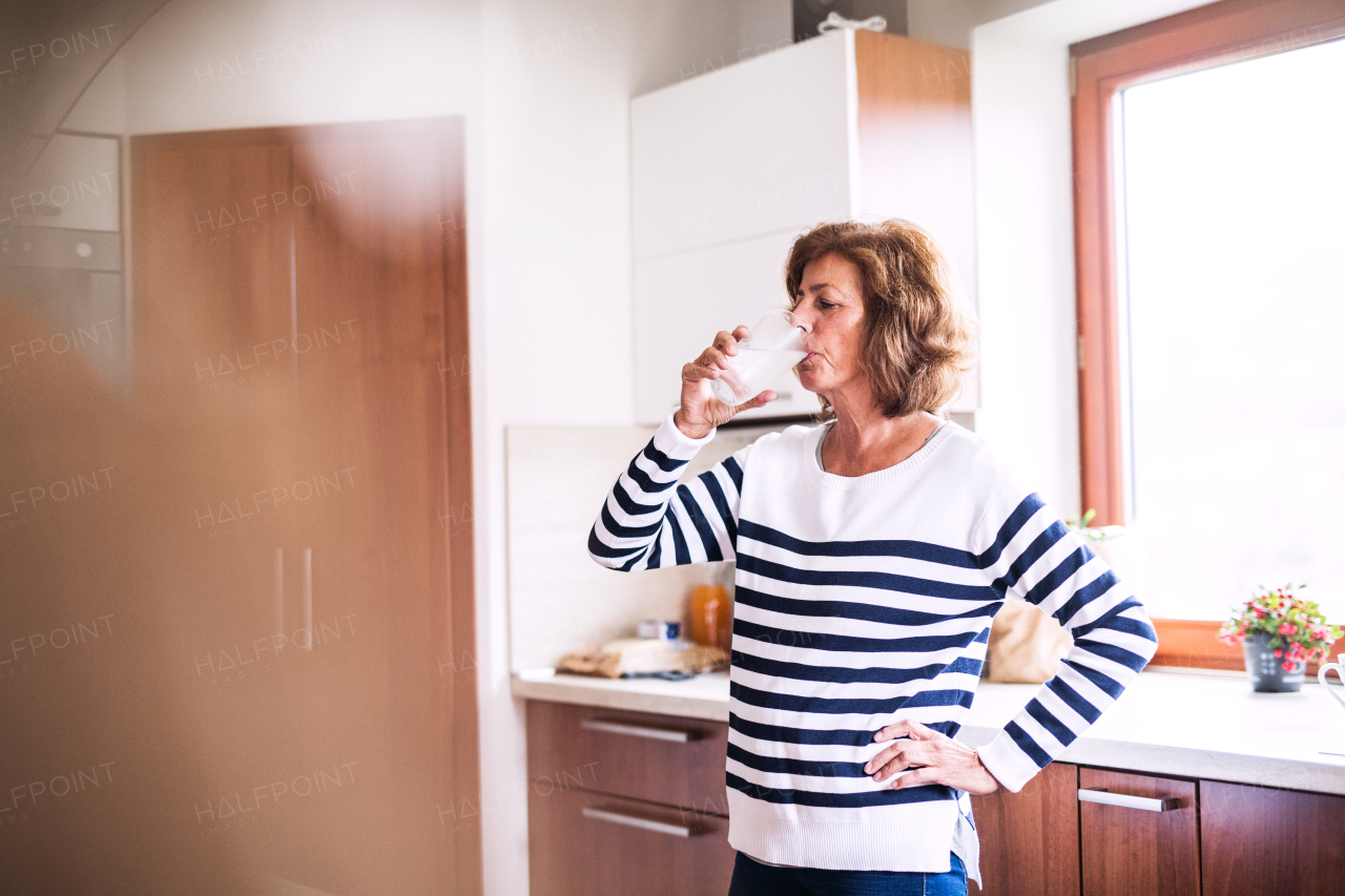 Senior woman in the kitchen. An old woman inside the house, drinking water.