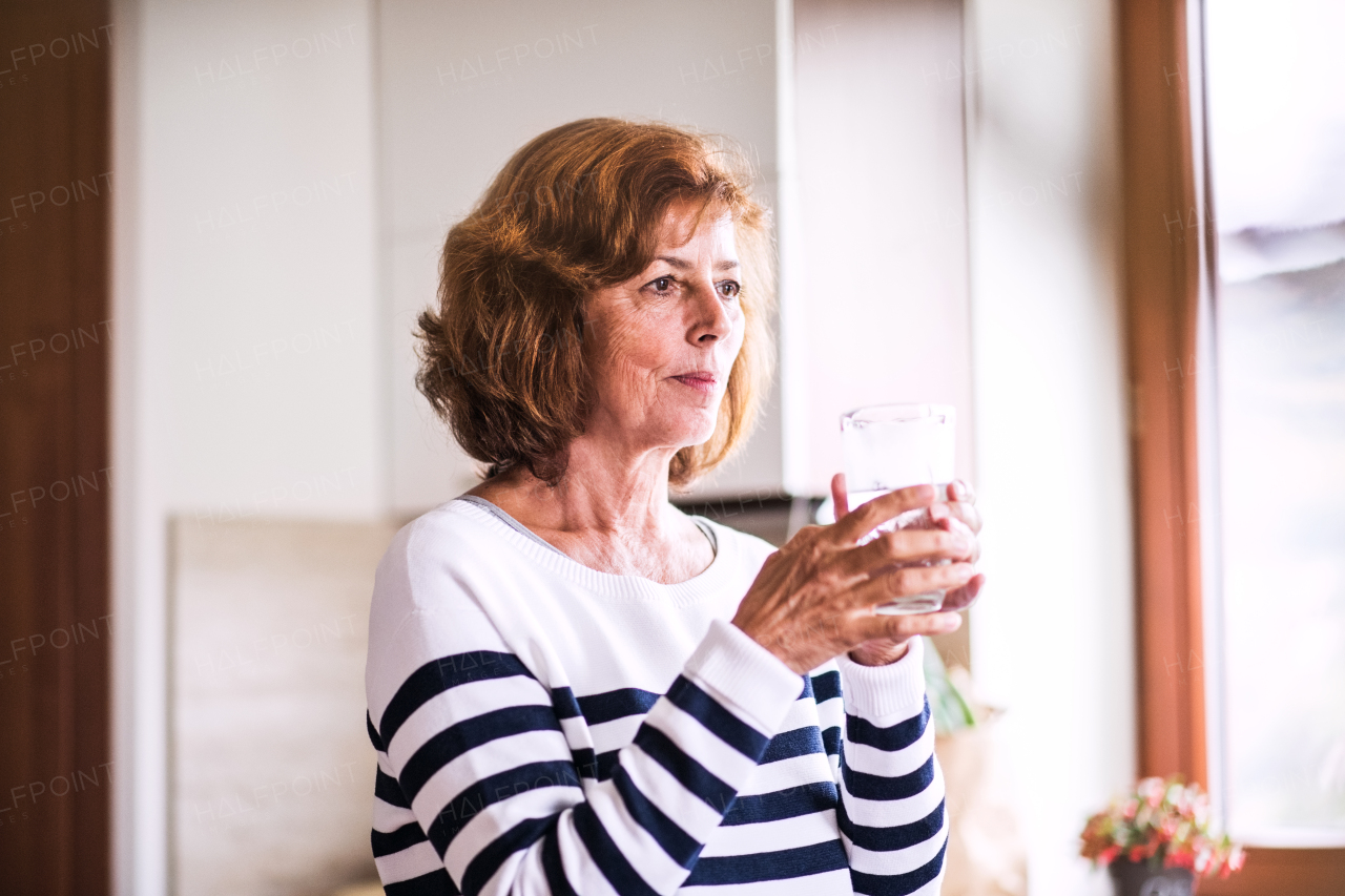 Senior woman in the kitchen. An old woman inside the house, holding a glass of water.