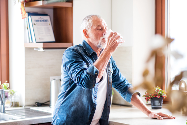 Senior man in the kitchen. An old man inside the house, drinking water.