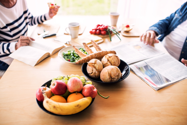 Unrecognizable senior couple eating breakfast at home. An old man and woman sitting at the table, reading.