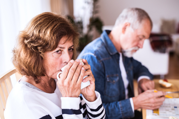 Senior couple relaxing at home. An old man and woman sitting at the table, drinking coffee and doing crosswords.