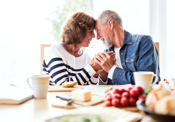 Senior couple eating breakfast at home. An old man and woman sitting at the table, holding hands.